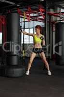 Muscular girl beating punching bag in hall