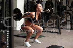 Beautiful girl exercising squatting with barbell