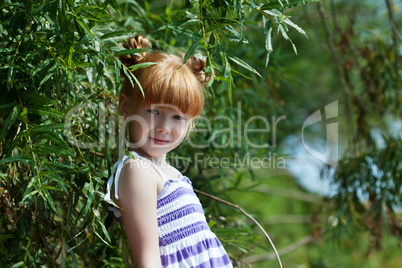 Cute red-haired little girl posing near tree