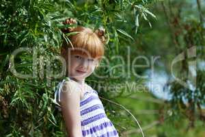 Cute red-haired little girl posing near tree