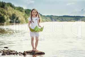 Adorable girl posing with paper boat on lake