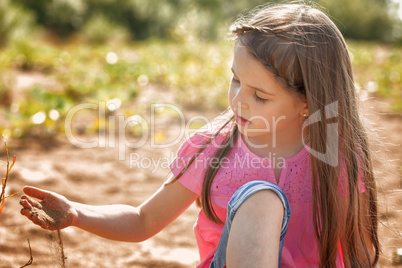 Cute girl thoughtfully playing with sand in park