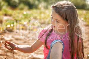 Cute girl thoughtfully playing with sand in park