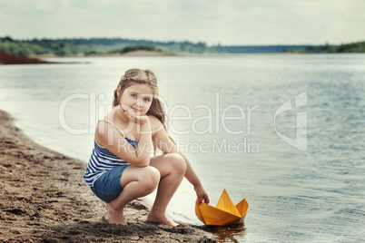 Cute girl posing with homemade paper boat by lake