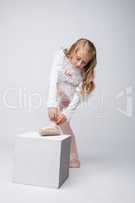 Curly little girl tying pointe, on gray backdrop