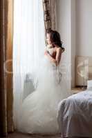 Half-dressed bride looks thoughtfully at window