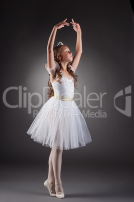 Sweet little ballerina posing on gray backdrop