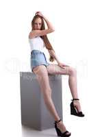 Long-legged slim girl sitting on cube