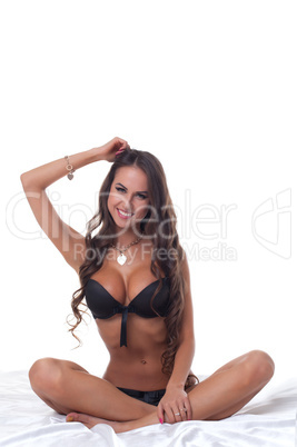 Smiling slim girl posing sitting on bed in studio