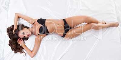 Model in erotic lingerie lying on silk bedsheet
