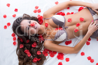 Cute lingerie model posing in bed with rose petals
