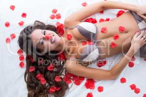 Cute lingerie model posing in bed with rose petals