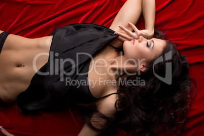 Top view of seductive brunette lying on red sheet