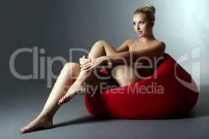 Beautiful naked woman sitting on red pouf