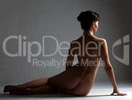 Rear view of nude slim brunette sitting in studio