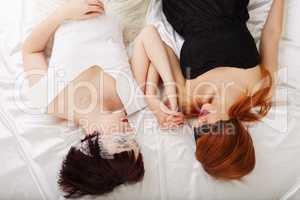 Sensual girls holding hands while lying in bed
