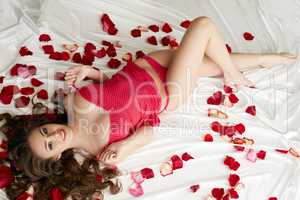 Sexy underwear model lying in bed with rose petals