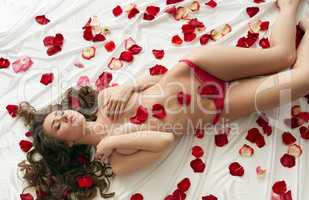 Topless girl posing in bed with rose petals