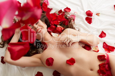 Happy naked girl lying in bed with rose petals