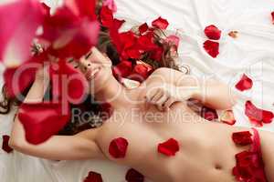 Happy naked girl lying in bed with rose petals