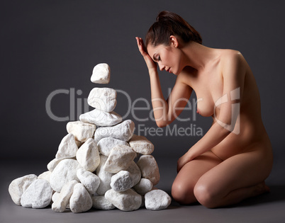 Nude woman telekinetically moving stones in studio