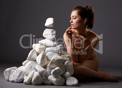 Naked woman thoughtfully moves stones by look