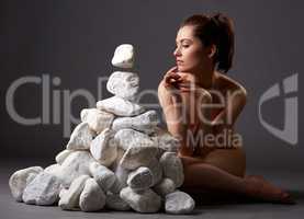 Naked woman thoughtfully moves stones by look