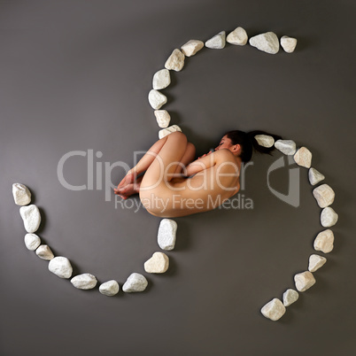 Top view of naked woman curled up with stones