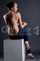 Topless model posing sitting on cube. Back view