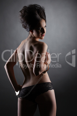 Rear view of topless skinny brunette in handcuffs