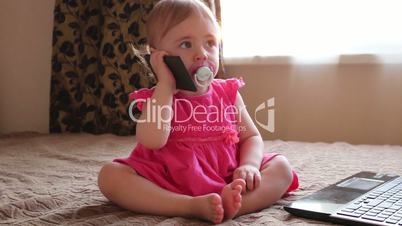 small kid plays with smartphone sitting on couch near window