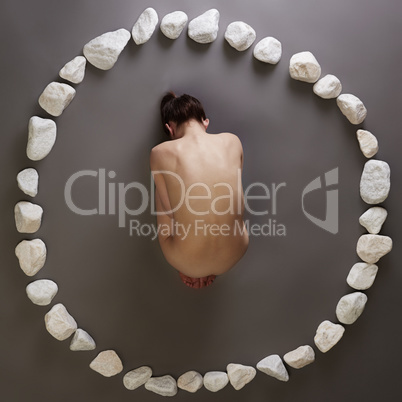 Naked girl lying in circle of stones. Top view