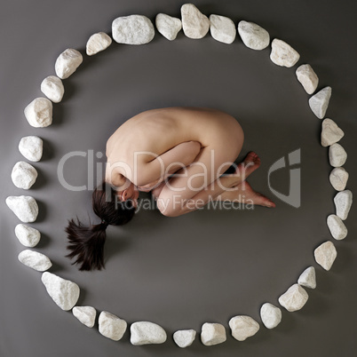 Nude woman lying in circle made of stones