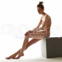 Languid naked model sitting on cube