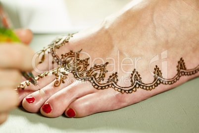 Mehendi. Master applying henna on model's leg