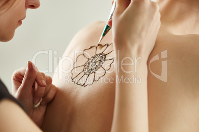 Mehndi master drawing with henna on model's back