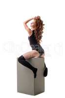 Sexy red-haired girl posing while sitting on cube