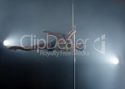 Strong girl dancing on pole in rays of spotlights