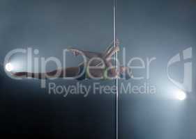 Strong girl dancing on pole in rays of spotlights