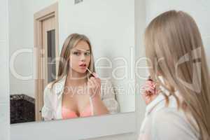 Reflection in mirror of sexy girl paints her lips