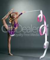 Cute gymnast dancing with ribbon, on gray backdrop