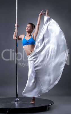 Elegant dancer posing at pylon, on gray background