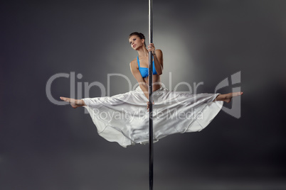 Flexible pretty girl dancing on pole in studio