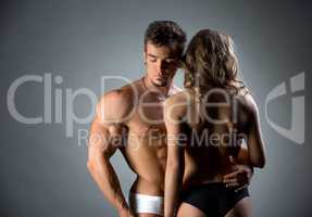 Muscular hunk embracing topless model by waist