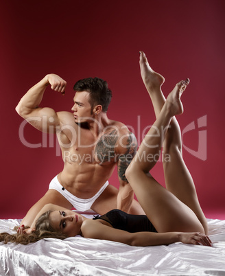 Sexy bodybuilder posing in bed with leggy model