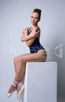 Tanned ballerina posing while sitting on cube