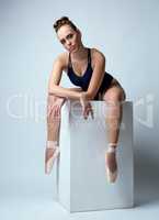 Ballerina posing with her legs dangling from cube