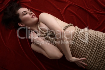 Shibari. Sexy woman lies on velvet bedsheet