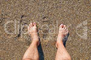 Male bare feet standing on the wet sandy beach