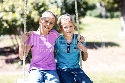 Siblings sitting on a swing in the park